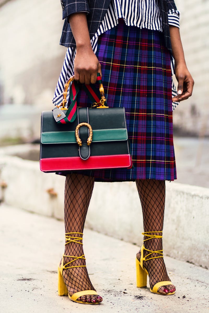 Fashion-forward outfit with plaid skirt and colorful handbag in urban setting.